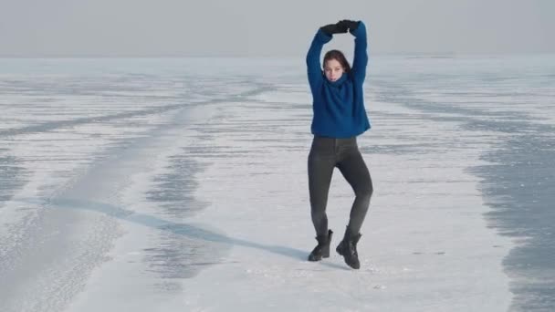 穿着毛衣、专业舞蹈演员、穿着时髦的年轻女子，在寒冷的冬天，在结冰的湖面上跳着精力充沛的爵士舞。在白雪覆盖的河流上，女性嬉皮士在社交网络上跳舞的挑战 — 图库视频影像