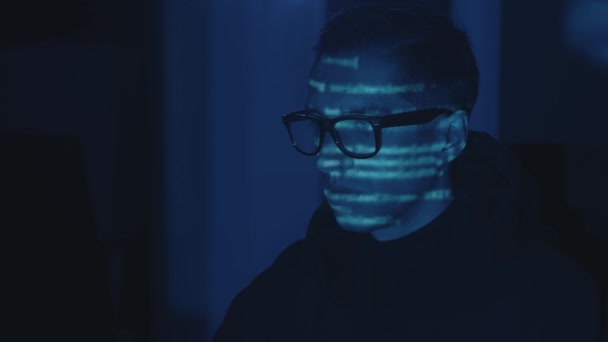 Portrét vývojáře počítačových hackerů v brýlích pracující počítač, kybernetický útok na server v noci. Programový kód se odráží na tváři. Nebezpečný mužský virtuální špion hacking software v tmavé místnosti — Stock video
