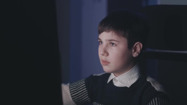 12-13 yaşlarında bir çocuk gece evde bilgisayar kullanıyor. Çocuk internetten öğreniyor. Anaokulu öğrencisi video izliyor ve online eğitim sırasında bilgisayar uygulamaları kullanıyor. Yüzündeki ışık yansımasını izle — Stok video