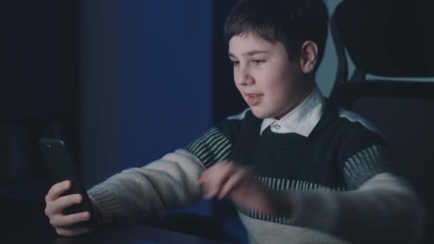 Smilende dreng 13 år gammel gør videoopkald ved hjælp af smartphone, mens du sidder hjemme sent om natten. Teenage skoledreng har en online videochat i stuen om natten, fjernkommunikation. – Stock-video