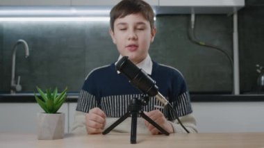 Çocuk vlogger kameraya bak ve internet için podcast videosu kaydet. Çocuk video blogcusu evde profesyonel mikrofonla video kaydediyor. Genç blogcu video çekiminde konuşuyor.