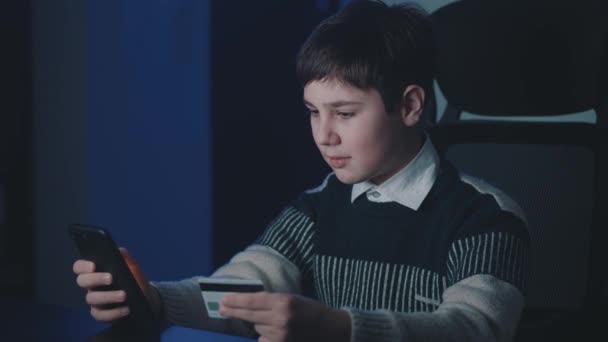 12-13 ετών αγόρι ψώνια σε απευθείας σύνδεση με πιστωτική κάρτα και smartphone, ενώ κάθεται στο σπίτι αργά το βράδυ. Παιδί σχολιαρόπαιδο με κινητό τηλέφωνο που χρησιμοποιεί online συστήματα πληρωμών. Τραπεζική on line. — Αρχείο Βίντεο