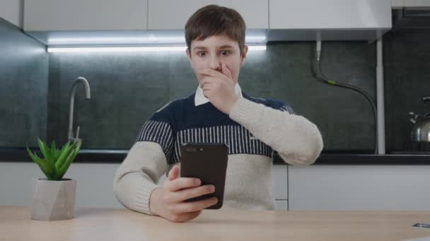 Φοβισμένο και σοκαρισμένο αγόρι δούμε οθόνη smartphone, καλύπτουν το στόμα με το χέρι στο σπίτι κουζίνα. Παιδί του σχολείου φοβάται τα κακά νέα, διαβάστε τρομερό μήνυμα στο κινητό τηλέφωνο στο σαλόνι. Βλέποντας βίντεο τρόμου — Αρχείο Βίντεο