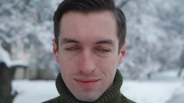 Nahaufnahme Porträt eines jungen Millennial-Mannes im Pullover, der in die Kamera blickt, im Freien auf winterlich verschneitem Hintergrund. — Stockvideo