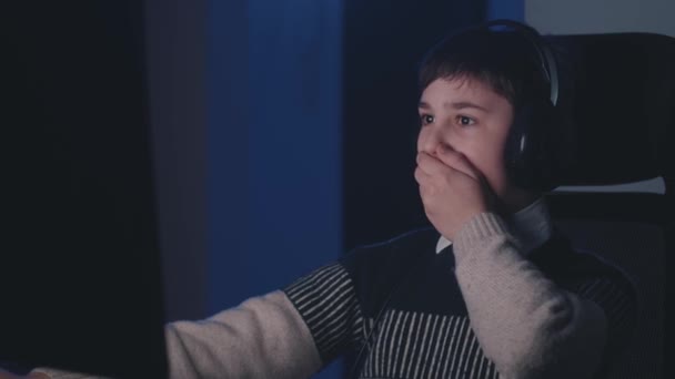 Φοβισμένο αγόρι με ακουστικά σοκαρισμένο από τρομερή σκηνή, ενώ βλέποντας βίντεο τρόμου στον υπολογιστή. Φοβισμένο σχολιαρόπαιδο κοιτάζει οθόνη οθόνη, καλύπτουν το στόμα με το χέρι του, ενώ χρησιμοποιώντας φορητό υπολογιστή αργά το βράδυ — Αρχείο Βίντεο