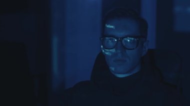 Gözlüklü bilgisayar programcısı portresi, geceleri sunucuya siber saldırı. Program kodu yüze yansıdı. Tehlikeli erkek sanal casus hackleme yazılımı karanlık odada
