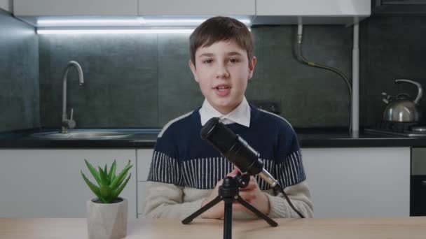 男の子vloggerは、カメラを見て、インターネット用のポッドキャストビデオを記録します。子供のビデオブロガーは自宅でプロのマイクで新しいvlogビデオを撮影.若いブロガービデオ撮影について話す. — ストック動画
