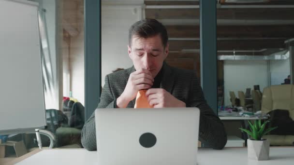 Businessman suffering with allergies in an office. Sick male in suit working on laptop at his office, feeling sneezes and has a runny nose, symptoms of flu and cold. — Stock Video