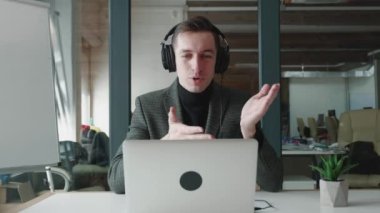 Ofiste otururken bilgisayarı kullanarak kulaklık takan gülümseyen bir iş adamı. Video görüşmesinde konuşan yakışıklı bir adam. Webcam şirketi toplantı konsepti.