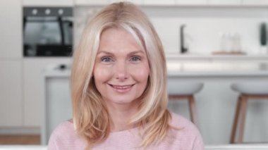 Mutlu, olgun orta yaşlı bir kadının, evde kameraya bakıp, gülümseyen yaşlı, gri saçlı bir kadının portresi sağlıklı, mutlu, emekli, güzel bir yüz resmi olan yaşlı bir kadının fotoğrafı.