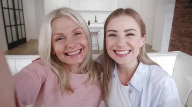 Mutlu, olgun bir anne ve yetişkin bir kız evdeki rahat koltukta otururken cep telefonuyla selfie çekiyor..