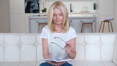 Stresli olgun bir kadın kitap okumayı bırakır çünkü baş ağrısı çeker ve evdeki kanepede oturur. Yorgun, yaşlı, sarışın kadın. Okuduktan sonra gözlüğünü çıkarıyor..