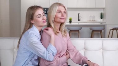 Güzel, gülümseyen, yetişkin kızıyla birlikte evdeki kanepede oturan ve birlikte vakit geçirmenin tadını çıkaran bir anne. Aile sevgisi kavramı.