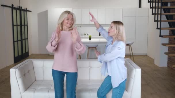 Щаслива сім'я старша мама розважається з дорослою дочкою танцює у вітальні, безтурботна стара мама з дорослою дочкою сміється, насолоджуючись кумедною активністю вдома — стокове відео