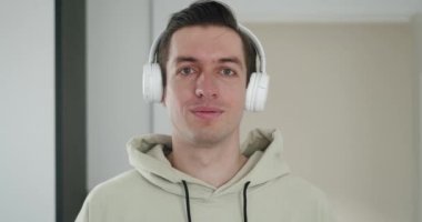 Beyaz kulaklıklı şık bir adamın portresi müzik dinliyor ve kapalı alanda kameraya bakıyor.