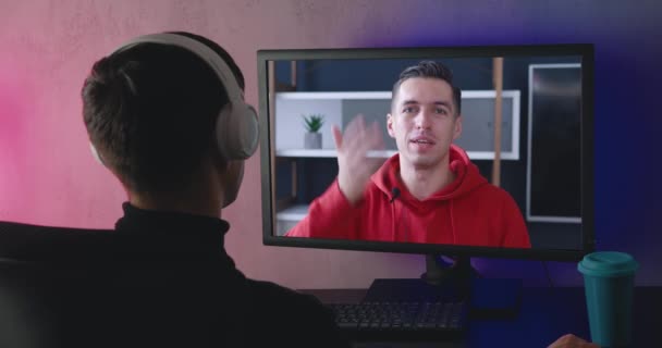 Achteraanzicht van een jongeman met koptelefoon die een videoblog kijkt, binnen. Achteraanzicht van een mannelijke student kijkt 's avonds thuis een trainingsvideo, een online webinar op een computermonitor. — Stockvideo