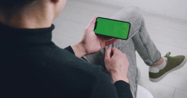 Arka görünüm, akıllı telefon kullanan, kaydıran, kaydıran ve sensör ekranında tıklayan, yeşil ekranı izleyen, cep telefonu krom anahtar yatay yönelimde eğlenen genç adam.