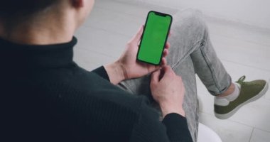 Arkadaki görünüm, akıllı telefon kullanan genç adam yeşil ekran izliyor cep telefonu kroma anahtar dikey gösterim keyfi, kapalı otururken