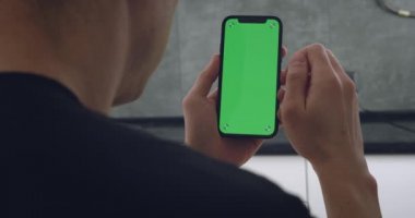 Arka görünüm, akıllı telefon kullanan, kaydıran, kaydıran ve sensör ekranında tıklayan, yeşil ekranı izleyen, cep telefonu kroma anahtar dikey yönelim görüntüsü 4k