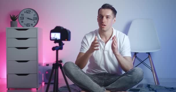 Πορτρέτο του αρσενικού videoblogger γυρισμάτων νέο βίντεο vlog με επαγγελματική κάμερα, ενώ κάθεται στο πάτωμα στο σπίτι — Αρχείο Βίντεο