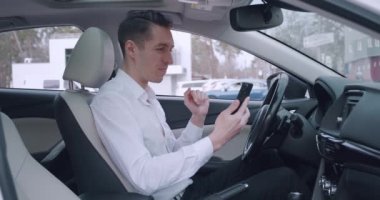 Genç iş adamı arabada otururken akıllı telefon kullanarak görüntülü konuşma yapıyor. Erkek sürücü cep telefonuyla video görüşmesi yapıyor..