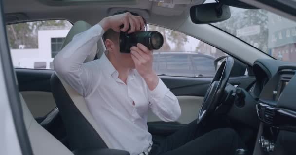 Homme avec caméra assis à l'intérieur de la voiture et de faire des photos avec caméra professionnelle, détective privé ou paparazzi espionnage. — Video