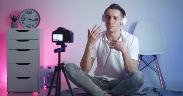 Homem blogueiro feliz em fones de ouvido filmando novo vídeo vlog com câmera profissional enquanto sentado no chão em casa. Criador de conteúdo masculino filmando aulas online. — Vídeo de Stock