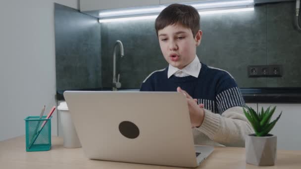 Evde masada otururken bilgisayarla görüntülü konuşma yapan gülümseyen çocuk. Kulaklıklı öğrenci evden online dersler izliyor. Uzaklık öğrenimi — Stok video