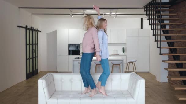 Happy family senior mom having fun with adult daughter dancing on sofa in living room. Carefree old mother with grown daughter listening music, jumping on couch enjoy funny activity together at home. — Stock Video