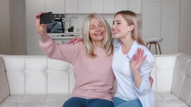 Boldog szerető érett anya és felnőtt lánya, hogy szelfi video hívást mobiltelefonnal, miközben ül a kényelmes kanapén otthon. — Stock videók