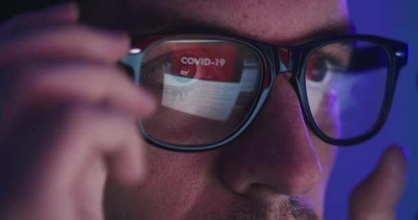 Close-up retrato de homem em óculos tarde da noite rolando notícias abous coronavirus na frente do laptop — Vídeo de Stock