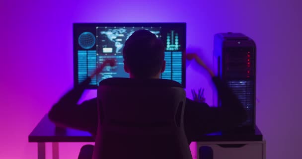 Задний вид человека программиста доволен успехом во время работы за компьютером в дата-центре ночью. Опасный хакер работает в центре кибербезопасности, заполненном неоновым светом. — стоковое видео