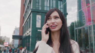 Şehir arka planında cep telefonu kullanan çekici genç bir iş kadını. Akıllı telefon kullanan ve şehir merkezinde duran güzel genç bir bayanın yüz portresini kapat. Gerçek insanlar..