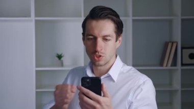 Şaşırtıcı iş adamı kazananı akıllı telefonu tutuyor. Evde oynanan online bahis oyununun kazanmasından hayrete düşen iyi haberleri okuyor. Başarılı erkek girişimci, cep telefonuna bakarak zafere seviniyor