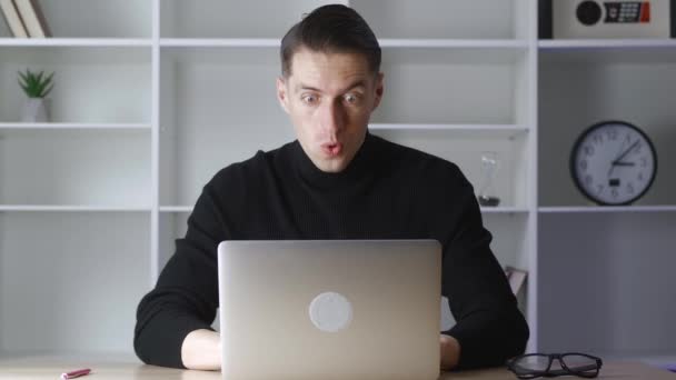 El hombre de negocios exitoso se sienta a la mesa con el ordenador portátil trabajando en la oficina. Recibe buenas noticias y está encantado. Feliz ganador masculino celebrar el éxito de ganar y mostrar sí gesto — Vídeos de Stock