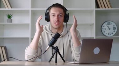 Yakışıklı genç blogger mikrofonla konuşan ve ofisteki kameraya bakan ses kaydı yapıyor. Erkek vlog kaydedicisi ofisindeki iş yerinde video blogu kaydediyor.
