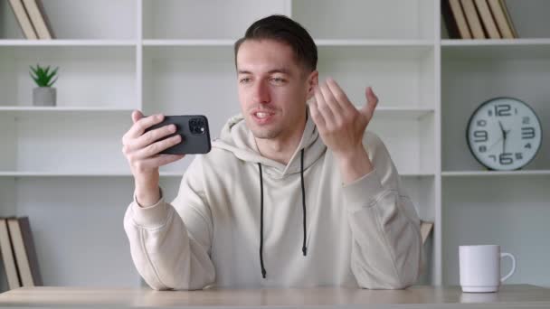 Modern ofisteki akıllı telefonuyla görüntülü konuşma yapan mutlu bir adamın portresi, telefon ekranındaki insanlara el sallıyor. Genç erkek blogcu cep telefonu kullanarak video bloğu yapıyor — Stok video