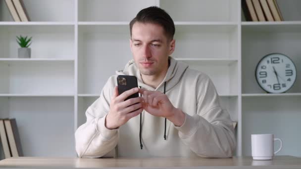 Άνδρας επαγγελματίας κρατώντας μήνυμα SMS smartphone στο γραφείο. Νεαρός ελεύθερος επαγγελματίας επιχειρηματίας που χρησιμοποιεί εφαρμογές για φορητές συσκευές για τη διαχείριση του επιχειρηματικού χρόνου έννοια κάθεται στην εργασία. Χρήση κοινωνικών δικτύων. — Αρχείο Βίντεο