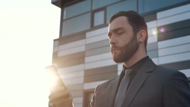 Κάμερα περιστρέφεται γύρω από ελκυστική αυτοπεποίθηση επιχειρηματίας CEO χρησιμοποιώντας το smartphone app στέκεται κοντά στο σύγχρονο κτίριο γραφείων. Άνδρας επαγγελματίας που χρησιμοποιεί κινητό τηλέφωνο. Φορώντας κλασσικό κοστούμι. Κοινωνικό δίκτυο. — Αρχείο Βίντεο
