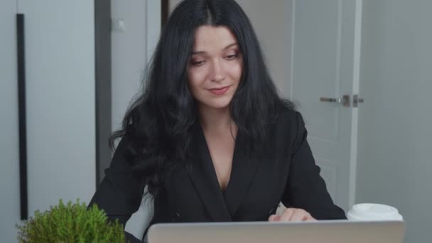 La mujer está usando el portátil mientras está sentada en su escritorio y bebiendo café. La joven empresaria europea está sentada en la oficina y trabajando en software informático. Steadicam tiro. — Vídeos de Stock