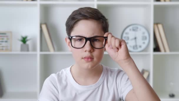 Przestraszony i zszokowany 13-latek w białej koszuli zdejmuje okulary i zakrywa usta dłonią. Zaskoczony dzieciak nastolatek boi się złych wieści patrząc w kamerę na tle domu. — Wideo stockowe