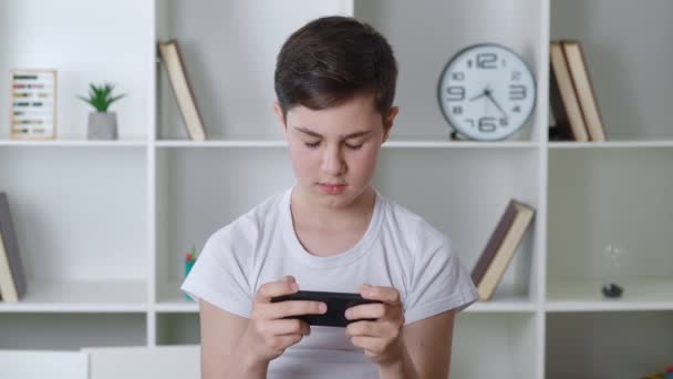 Knappe jongen van 13 jaar oud spelen mobiel spel op de smartphone thuis. Tiener speelt mobiele telefoon. Hij gebruikt telefoon om te gamen. Kind spelen van video game binnen — Stockvideo