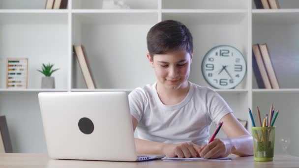 Pre-Teen gutaussehenden Schüler besuchen zu Hause Online-Schulklasse auf seinem Computer-Laptop wegen covid-19 und Notizen auf Notebook schreiben. Fernunterricht Online Learning Lektionskonzept — Stockvideo