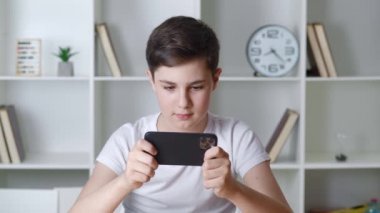 13 yaşında güzel bir çocuk evde akıllı telefondan oyun oynuyor. Cep telefonuyla oynayan bir genç. Çocuk oyun oynamak için telefonu kullanıyor. İçeride video oyunu oynayan çocuk