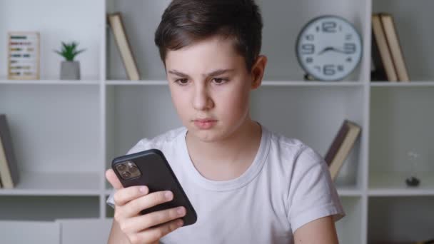 Portrét třináctiletého chlapce používá smartphone, když sedí doma. Fešák teenager surfování na internetu s mobilním telefonem, pomocí e-learning aplikací — Stock video