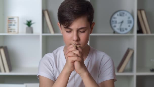13-letni chłopiec wypowiada życzenie modli się koncepcja religii. Zaufanie do Boga, modlitwa męskie dziecko z nadzieją w sercu i ze złożonymi ramionami, módl się do Boga siedzącego przy biurku w domu. — Wideo stockowe