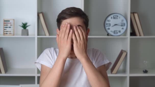 Retrato de un niño asustado, ve lo terrible y cubre su rostro con sus manos horrorizadas. Chico viendo una película de terror y se asusta mientras se sienta en casa — Vídeos de Stock