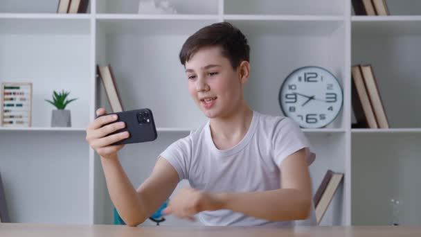 13 yaşındaki bir çocuk evde otururken akıllı telefon kullanarak video görüşmesi yapıyor. Genç öğrenci oturma odasında görüntülü konuşma yapıyor. Uzaktan iletişim.. — Stok video