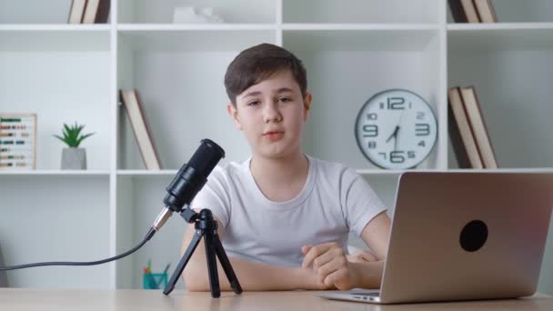 Chlapec vlogger se dívá na kameru a nahrává podcast video pro internet. Kid videoblogger natáčí nové video s profesionálním mikrofonem doma. Mladý blogger mluví o natáčení videa. — Stock video