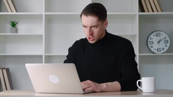 Angry mad businessman is showing aggression while working on a laptop in the office. Aggressive man shouts at coworkers remotely via video chat, sitting at desk indoors — Stock Video